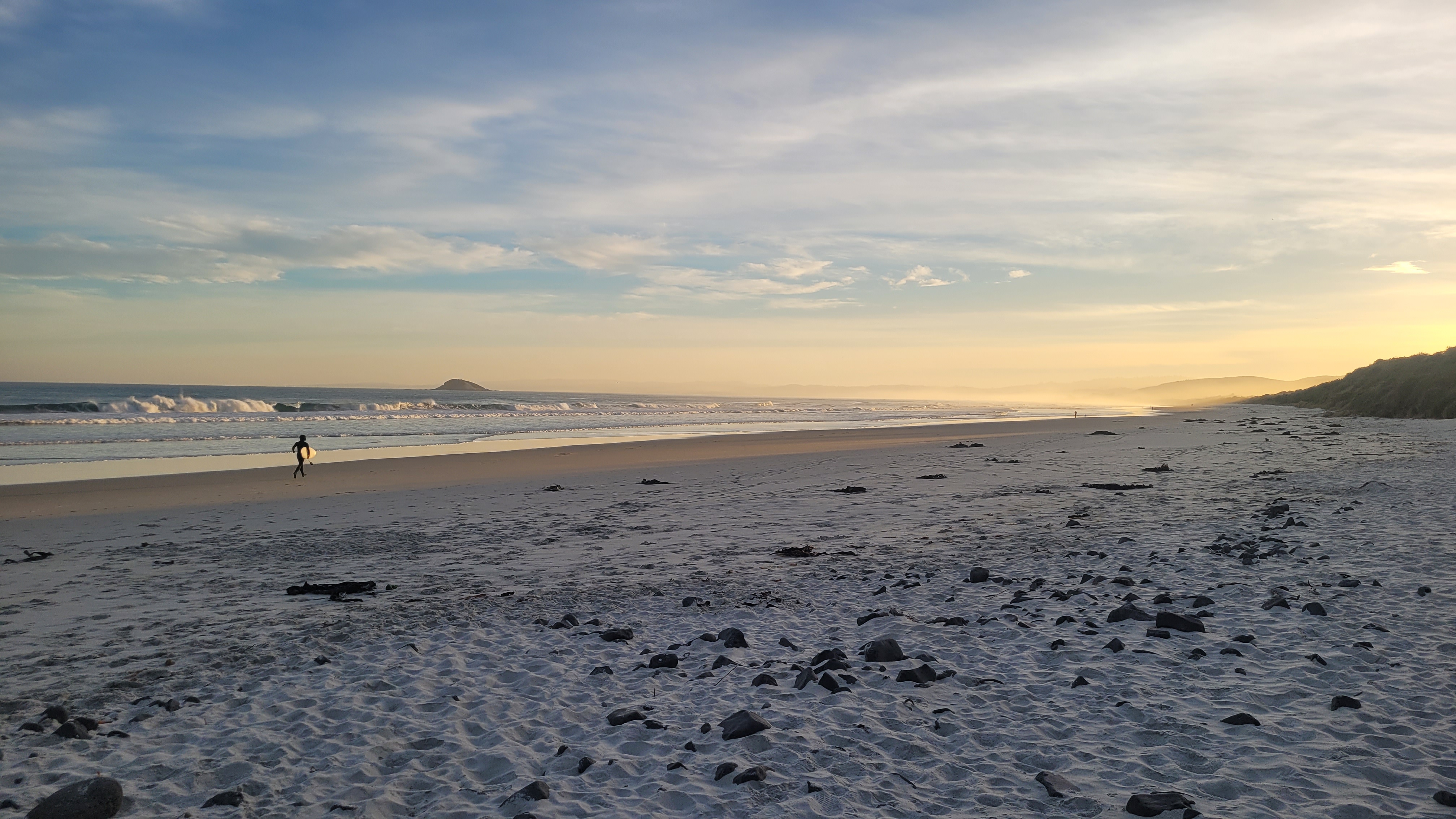 Empty sandy beach at sunset with a single surfer